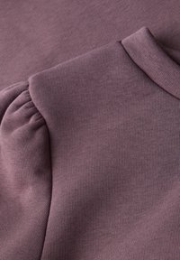 Nahaufnahme von mauvefarbenem, geripptem Stoff mit gepolsterten Schulternähten und Stehkragen-Detail an einem Kleidungsstück.