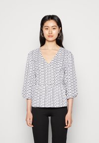 Blusa com padrão branco e preto, decote em V, mangas três-quartos e cintura franzida. O tecido parece leve, com uma textura suave.