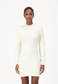 Abito bianco a maglia con texture a coste, collo alto e maniche lunghe a sbuffo, caratterizzato da una silhouette aderente e dettagli di pattern sottili.
