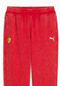 Röda svettbyxor med en mjuk textur, med en gul Ferrari-logotyp och en vit Puma-logotyp på vänster ben. Elastisk midja för komfort.