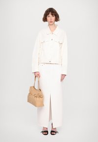 Άσπρο τζάκετ από τζιν, μακριά άσπρη φούστα με άνοιγμα, καφέ τσάντα με αλυσίδα ως χερούλι, μαύρες σανδάλες με διακοσμητικά στοιχεία.