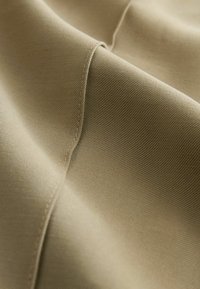 Nærbillede af beige stof, der viser en fin vævet tekstur og detaljeret syning langs en søm med bløde folder.