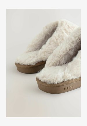 Pruunid platvormi sussid pehmete, paksude kreemivärvi kunstkarvadega ülemiste osadega, millel brändinimi "NEXT" on graveeritud taldmiseks.