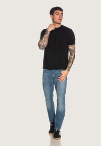 T-shirt nera a maniche corte con logo ricamato, abbinata a jeans skinny blu chiaro e sneakers nere con dettagli bianchi.