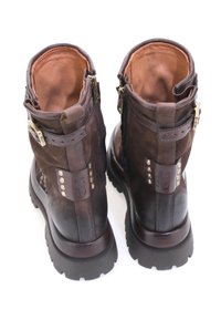 Smeđe kožne gležnjače s mat završetkom, koje imaju zlatne metalne dijelove, zakovice i robusnu podršku, prikazane sa stražnje strane.