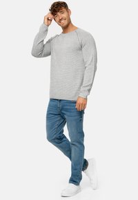Lys grå langærmet sweater med horisontale striber, parret med blå jeans og hvide sneakers. Har en rund halsudskæring og tekstureret stof.