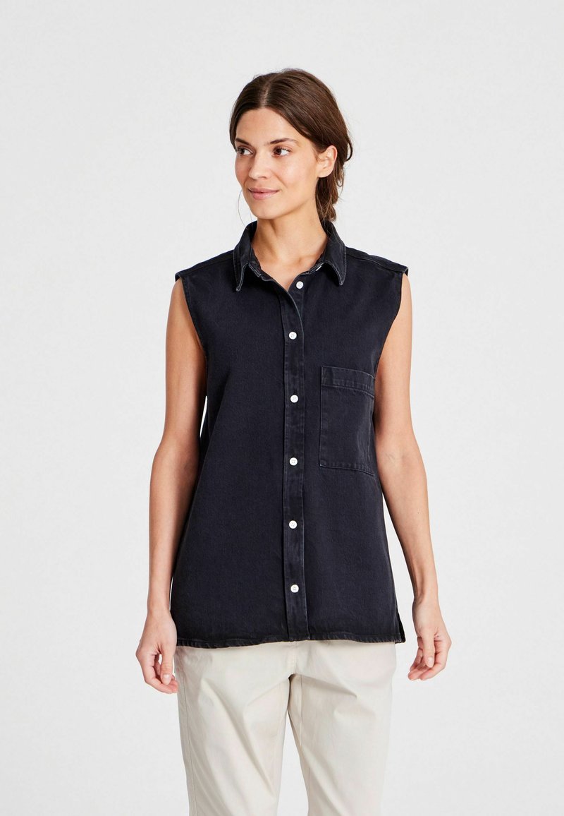 Camisa sin mangas de mezclilla oscura con cuello clásico, cierre de botones en la parte frontal y bolsillo en el pecho. Ajuste ligeramente relajado y textura suave.