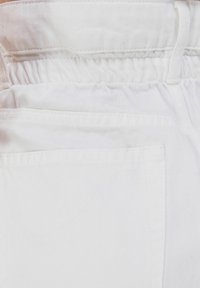 Vitt denimtyg med en veckad elastisk midja och flat fickor. Texturen är slät med ett subtilt twillvävsmönster.