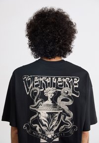 Black cotton t-shirt featuring graphic design with a central vase, serpent motifs, and vintage-style text on the back.