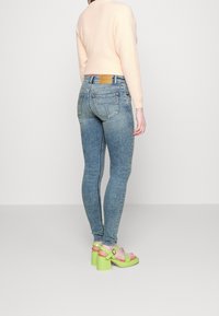 Hubené, světle modré džínové kalhoty s vybledlými detaily, spárované s pastelově růžovým svetrem a jasně zelenými sandály na blokovém podpatku.