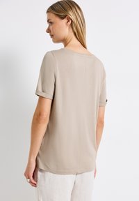 Vaaleanbeige lyhythihainen paita, jossa on väljä istuvuus, pyöreä kaula-aukko ja rullatut hihat. Ominaisuuksiin kuuluu suora helma sivuventtiileillä ja sileä pinta.