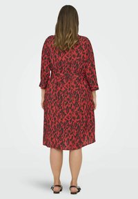 Rode en zwarte luipaardprint jurk met driekwartmouwen, een ceintuur in de taille en soepel vallende stof, die bij de achterkant knielang is.