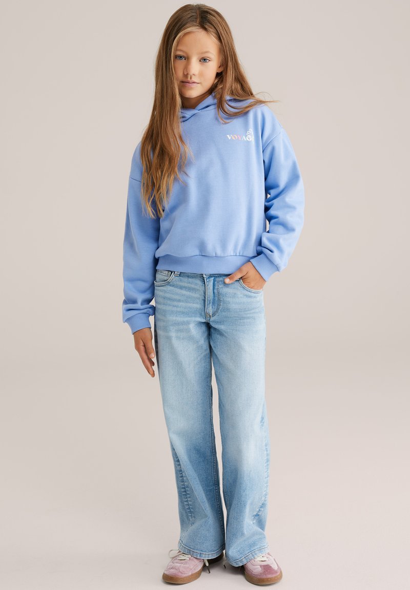 Sweat à capuche bleu clair avec un logo sur le devant, associé à un jean à jambes larges délavé clair et des chaussures roses. Texture lisse et design décontracté.