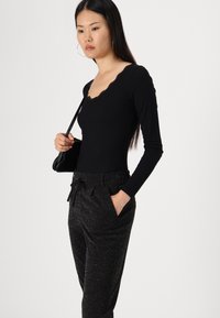 Top noir à manches longues côtelé avec un décolleté festonné, associé à un pantalon noir scintillant avec une taille à cordon et des poches latérales.
