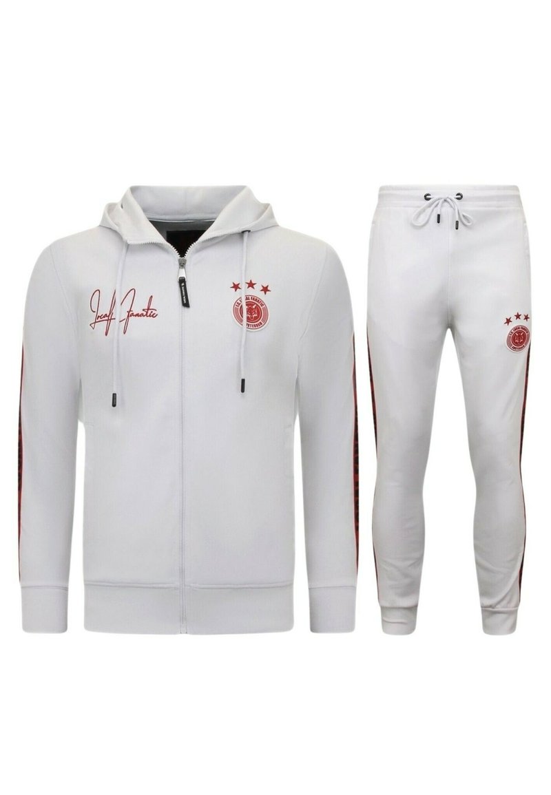 Witte trainingsoutfit met een rits-hoodie en joggingsbroek. Bevat rode accenten, een logo op de borst en gestreepte details aan de zijkant van de broek.