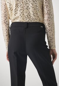 Pantaloni neri su misura con una trama liscia e una vestibilità elegante, abbinati a un top di paillettes dorate con un motivo scintillante.