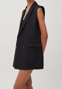 Black sleeveless blazer with double-breasted design, notched lapels, and two front pockets; smooth fabric with a structured silhouette.