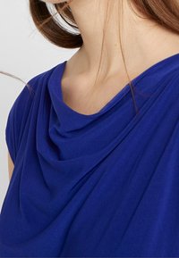 Top drappeggiato blu royal in tessuto morbido e leggero; scollatura tonda e pieghe sottili che creano texture e movimento.