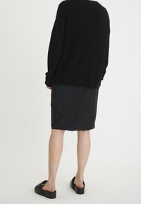 Svart fluffig tröja med avslappnad passform, kombinerad med en knälång svart blyertskjol och klumpiga svarta slidesandaler.