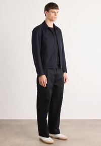 Casaco de marinheiro com fecho éclair na frente, gola pontuda e mangas longas, combinado com calças a condizer e ténis brancos com solas bege.