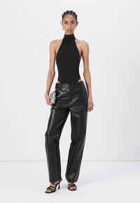 Czarny bodysuit bez rękawów z wysokim kołnierzem, połączony z luźnymi czarnymi spodniami skórzanymi. Modelka trzyma srebrną kopertówkę i ma na sobie sandały na obcasie.