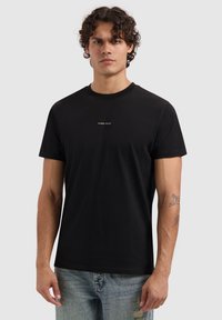 Zwarte katoenen T-shirt met een ronde hals, korte mouwen en een gouden "PURE PATH" logo in het midden op de voorkant. Eenvoudig ontwerp met een gladde textuur.