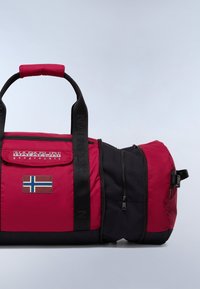 Punainen ja musta duffel-laukku vetoketjulla, kangaskahvat, Norjan lipun merkki ja kohokuvioitu logo hihnassa. Kompaktia ja kestävä muotoilu.