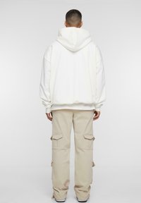 Hvid oversized hættebluse med en stor hætte, parret med beige cargo-bukser med flere lommer og en afslappet pasform.