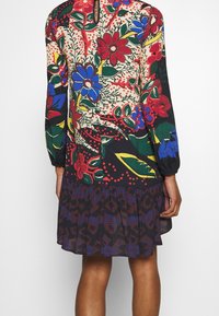 Jurk met bloemenpatroon, lange mouwen, een keyhole-achterkant en een gelaagde ruches zoom. Kleuren zijn onder andere rood, blauw, groen en zwart.