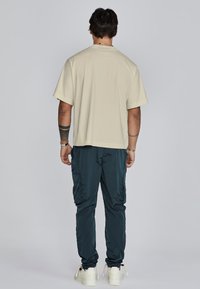 Beige T-shirt met korte mouwen en een ronde hals, gecombineerd met donkergroene cargobroek met zakken. Witte sneakers maken de look compleet.