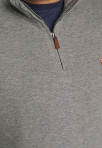 Grå zip hoodie i texturerat fleece-material. Har en läderdragkedja och en liten broderad design på br östet.