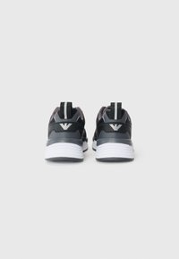 Zwarte en grijze sportschoenen met een textuurafwerking, witte zolen en een zwarte hielband met een logo. Minimalistisch ontwerp met een instapstijl.