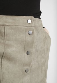 Gonna in tessuto scamosciato di un taupe attenuato con una finitura testurizzata. Presenta bottoni a pressione argentati lungo la parte anteriore e tasche laterali.