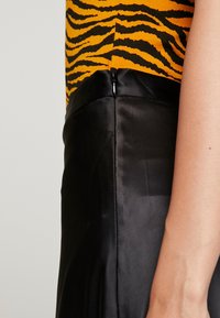 Schwarzer Satinrock mit glatter Textur, ausgestattet mit einem seitlichen Reißverschluss an der Taille und kombiniert mit einem auffälligen, orange-schwarz gestreiften Oberteil.