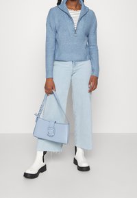 Ljusblå stickad tröja med halvdragkedja, tillsammans med ljusblå vida jeans och en rektangulär ljusblå läderhandväska.