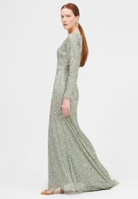 Langes, tailliertes Kleid in Hellgrün mit kunstvollen Perlenarbeiten und Pailletten. Lange Ärmel, runder Ausschnitt und ein fließender Rock.