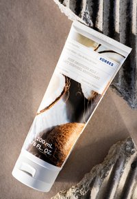 Witte knijpfles met bodylotion heeft een bruine kokosnoot op het label, met zwarte tekst en een witte schroefdop. Bevat 200 ml.