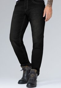 Jeans negros ajustados con costuras claras en contraste. Llevados con botas oscuras con cordones que presentan un diseño robusto y acentos texturizados.