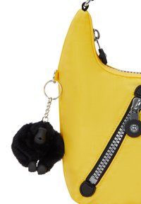 Bolso de hombro de nylon amarillo con detalle de cremallera negra y un charm de gorila peludo sujeto por una cadena. Textura suave y forma redondeada.