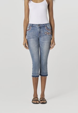 Lichtblauwe denim capri jeans met geborduurde accenten, mid-rise taille, slim fit en rafelige zoom bij de pijpen, gecombineerd met zwarte sandalen.