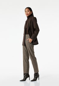 Brun blazer over en brun turtleneck, parret med hounds-tooth bukser og spidse sorte hæle. Glatte stoffer og skræddersyet pasform.
