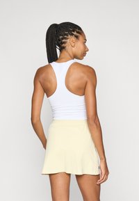 Vit atletisk linne med racerback-design, kombinerat med en ljusgul kjol i utsvängd modell, tillverkad av ett mjukt och stretchigt tyg.