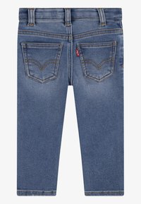 Jean en denim bleu avec une coupe droite, comportant deux poches arrière, des coutures orange et une petite étiquette logo rouge près de la poche droite.