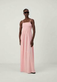 Robe maxi rose avec bretelles spaghetti, corsage froncé et tissu léger et fluide. Aucun motif ni détail en métal visible.