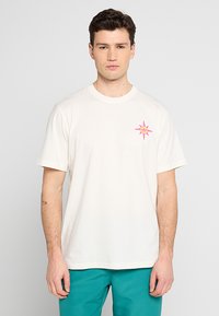 T-shirt in cotone color crema con scollatura rotonda e maniche corte. Presenta un design grafico di una stella rosa sull'area sinistra del petto.