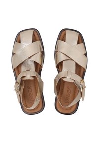 Sandalen met banden in metallic gouden leer, met gekruiste banden, gespsluiting en een bruine binnenzool. Vierkante neus met een platte zool.