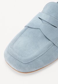 Heleda sinine sametist loafer, millel on ümar ruudukujuline varvas, iseloomulik õmblustamine ja dekoratiivne rihm peal. Pehme tekstuur ja õrn sära.