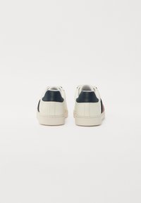 Valged nahast tossud on varustatud tumepunase kandmissegmendiga, punaste ja mustade küljeketšide ning tekstureeritud tallaga. Minimalistlik disain rõhutab mugavust.