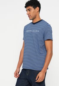 Tumed ja helesinine triibuline T-särk ümmarguse kaelusega, millel on rinnal valge "TOMMY JEANS" logo. Lühikesed varrukad.