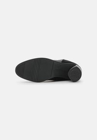 Semelle de chaussure en cuir noir avec une semelle en caoutchouc texturée, présentant des rainures horizontales et un accent de talon circulaire avec un détail de logo.